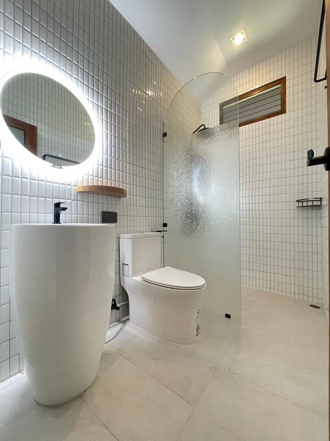 A modern bathroom with a large white sink, a toilet, and a shower with a glass door.