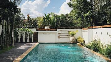 Una piscina rectangular con agua azul cristalina, rodeada por un muro blanco bajo y abundante vegetación.