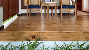 Una habitación con suelo de madera, dos sillas de mimbre, una mesita y una lámpara colgante.