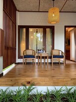 Quarto com piso de madeira, duas cadeiras de vime, uma mesa pequena e um lustre.