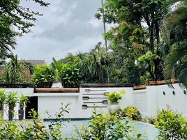 Área de piscina com parede branca, ripas de madeira e diversas plantas.