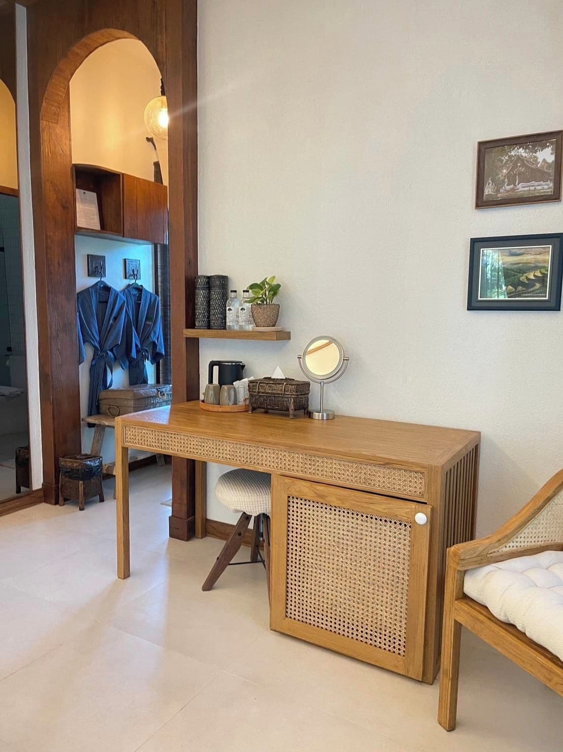 Une pièce comprenant un bureau en bois, une chaise, un petit tabouret, un miroir et un lit avec un matelas blanc.