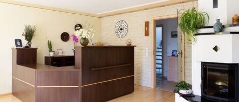 A reception desk with a clock, a fireplace, and a plant.