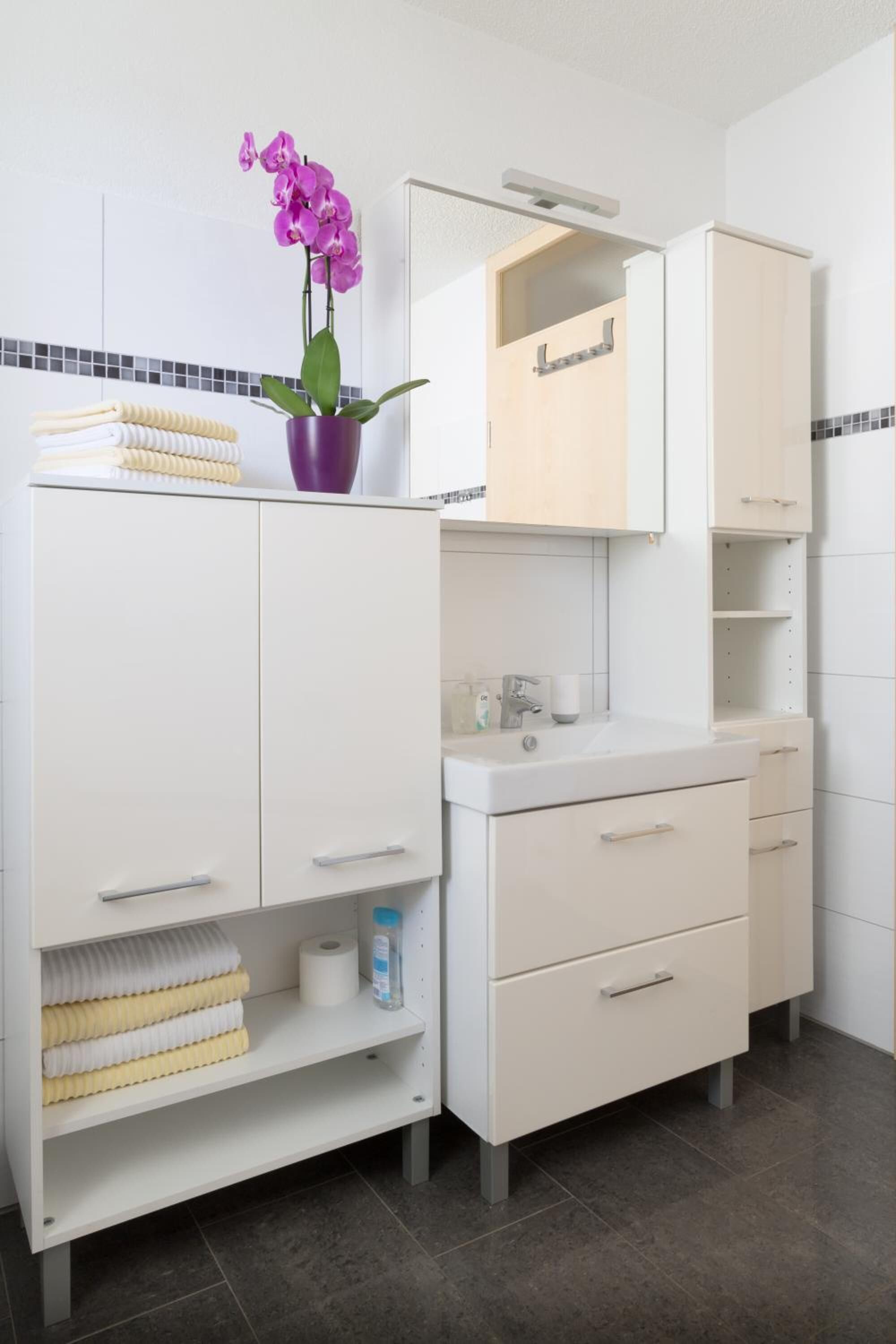A modern bathroom with white cabinetry, a mirror, and a purple orchid.