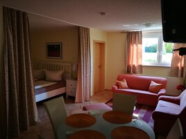 Una habitación acogedora con una cama, un sofá rojo, una mesa de comedor con sillas y una ventana con cortinas.
