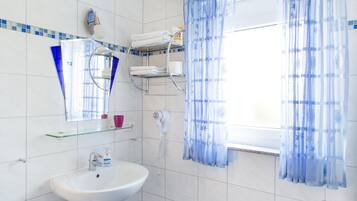 A bathroom with a white sink, a mirror, a towel rack, a hairdryer, and a window with blue curtains.