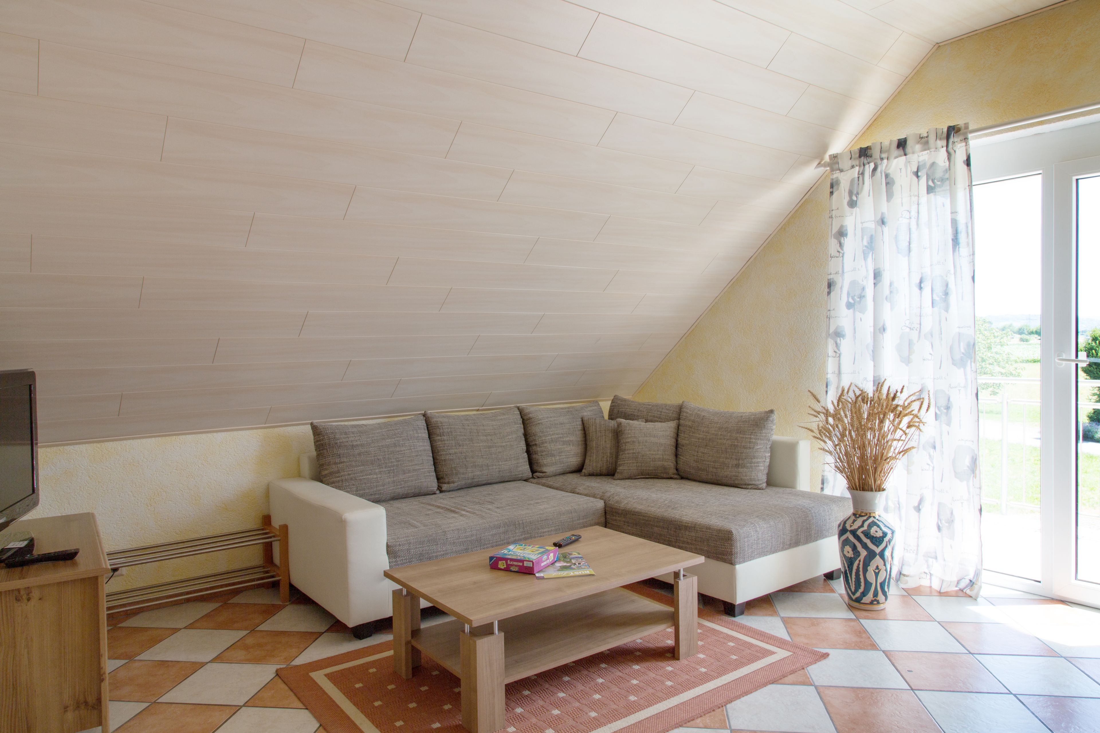 Ein modernes Wohnzimmer mit einem Ecksofa, einem Holztisch und einem großen Fenster mit Vorhängen.