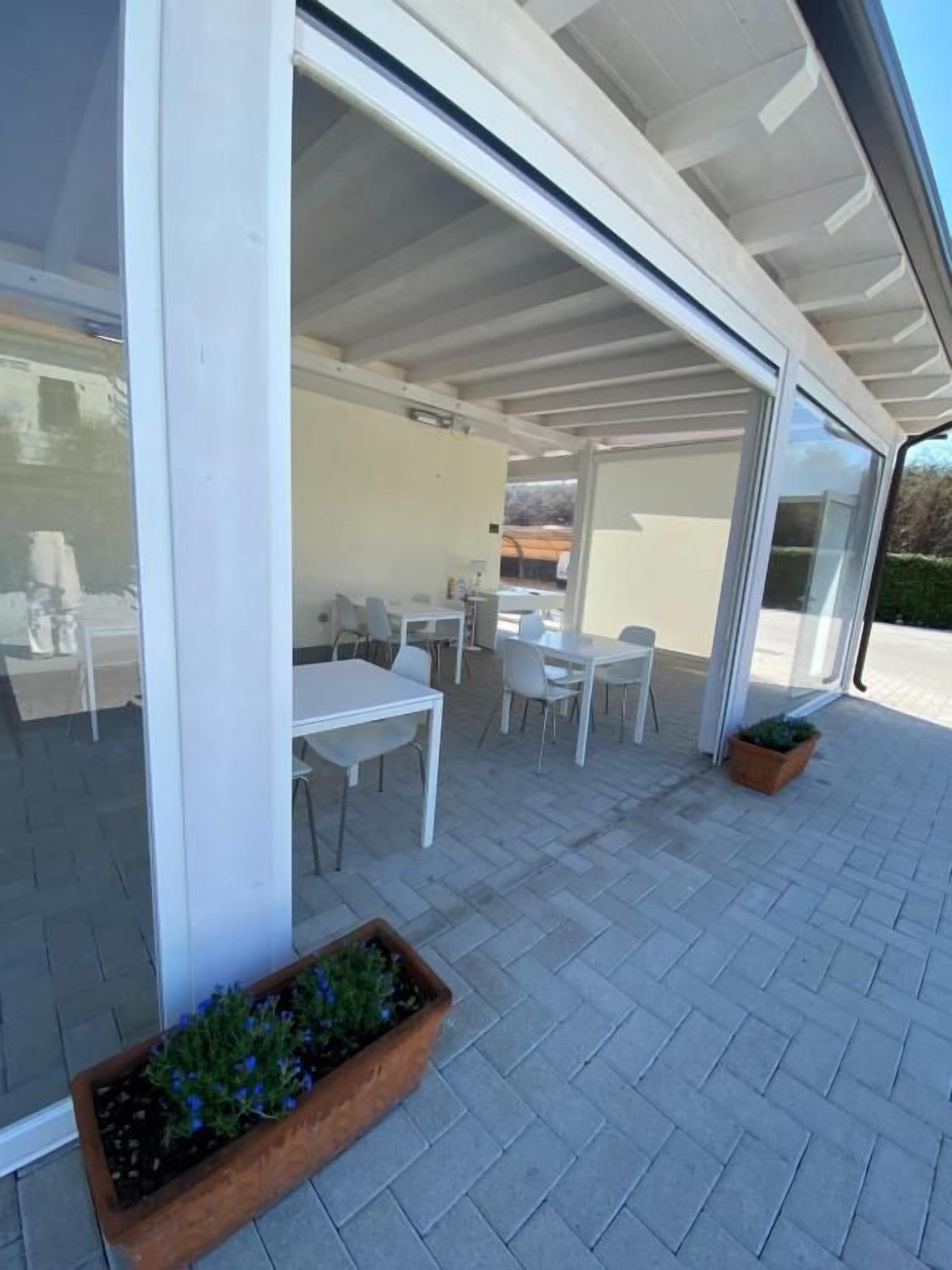 An outdoor patio area with a table and chairs, a planter with plants, and a glass door leading to an interior space.