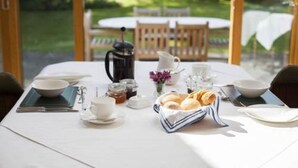 Una mesa de desayuno al aire libre con una cafetera, tetera, tazas y pasteles.
