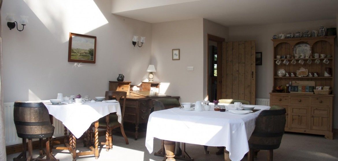 A dining area with two tables set for meals, wooden chairs, a wooden cabinet with dishes, and a painting on the wall.