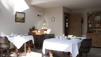 A dining area with two tables set for meals, wooden chairs, a wooden cabinet with dishes, and a painting on the wall.