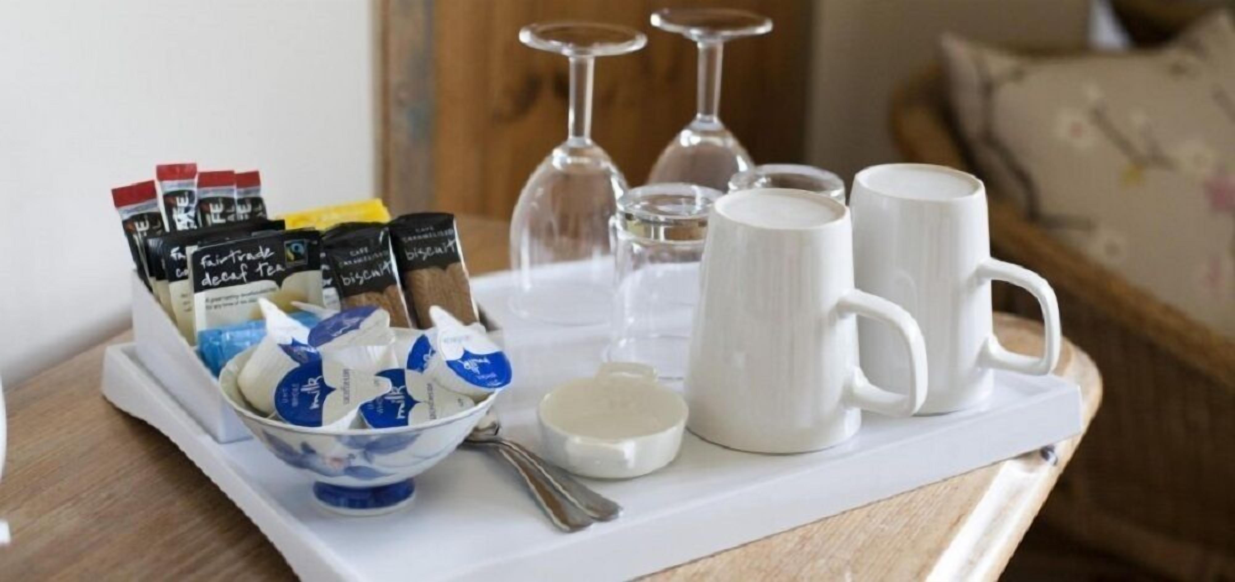 Een dienblad met koffiemokken, een schaal koekjes en theezakjes op een tafel.