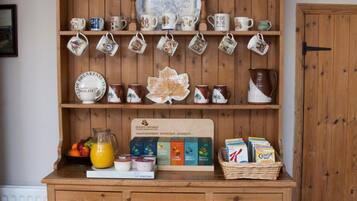 A wooden cabinet with shelves holding various kitchen items, including teapots, mugs, and a fruit bowl.