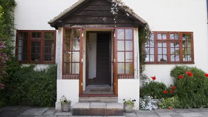 Una casa tradicional con puerta de madera, un pequeño porche y un jardín lleno de flores rojas.
