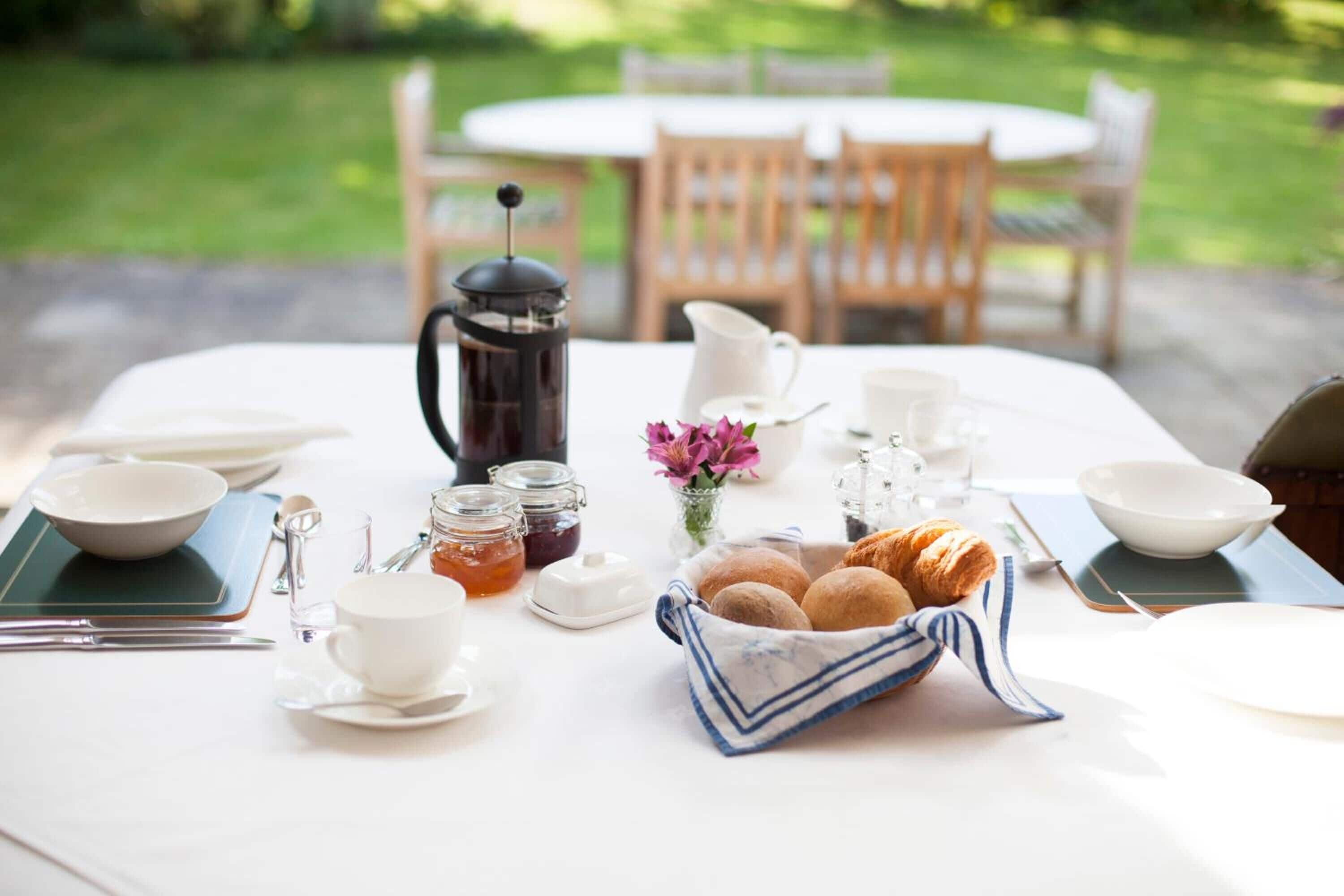 Mesa de desayuno al aire libre con una cafetera, pasteles y té.