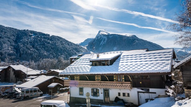 A snow-covered mountain village with traditional wooden buildings, a clear sky, and a prominent peak in the background.