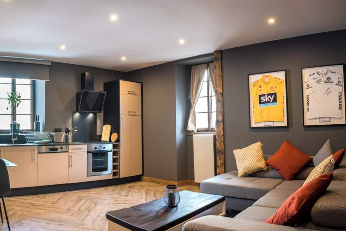 Una sala de estar moderna con sofá, una mesa de comedor con sillas, una zona de cocina con electrodomésticos y un ventanal grande.