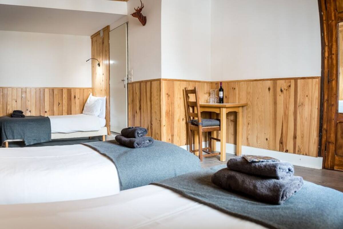 Una habitación con dos camas, paredes de madera, una mesita con una botella y una silla.