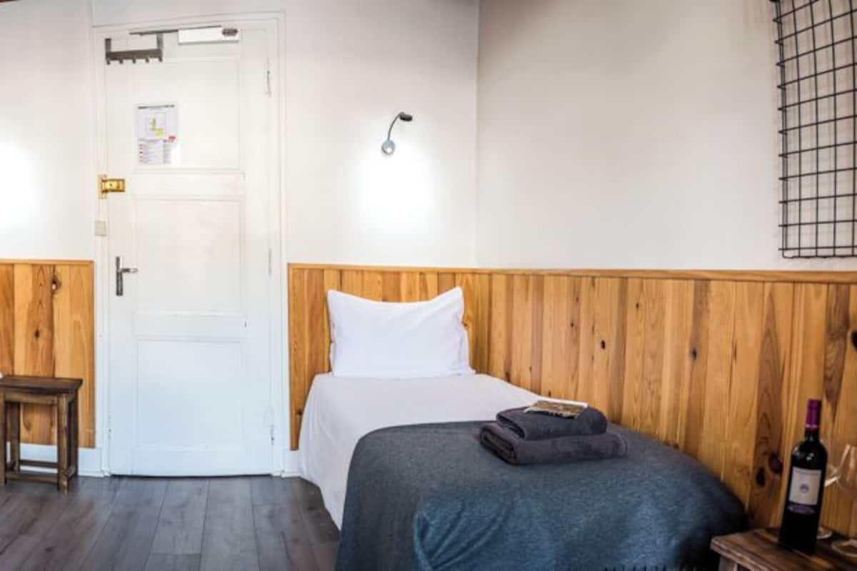 Una habitación con dos camas, cabeceros de madera, una mesita pequeña, una puerta blanca y una botella de vino sobre una mesita de noche.