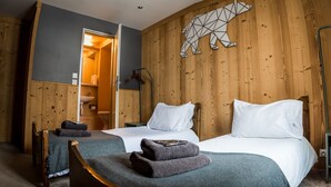 A room with two beds, wooden walls, a geometric animal wall art, and a visible bathroom.