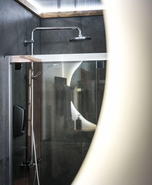 Une douche moderne dotée d’une paroi en verre, d’un pommeau de douche à main et d’un panneau de commande fixé au mur.