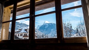 A window with a view of a snow-covered mountain and a building with a sloped roof.