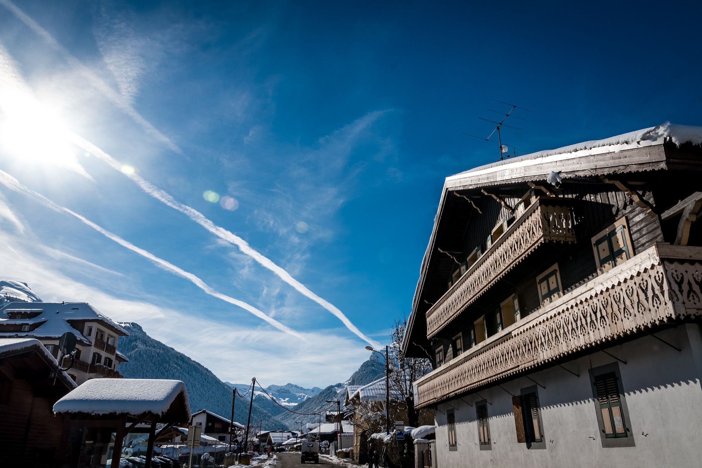 A traditional wooden building with balconies, a snow-covered mountain in the background, and a clear sky.