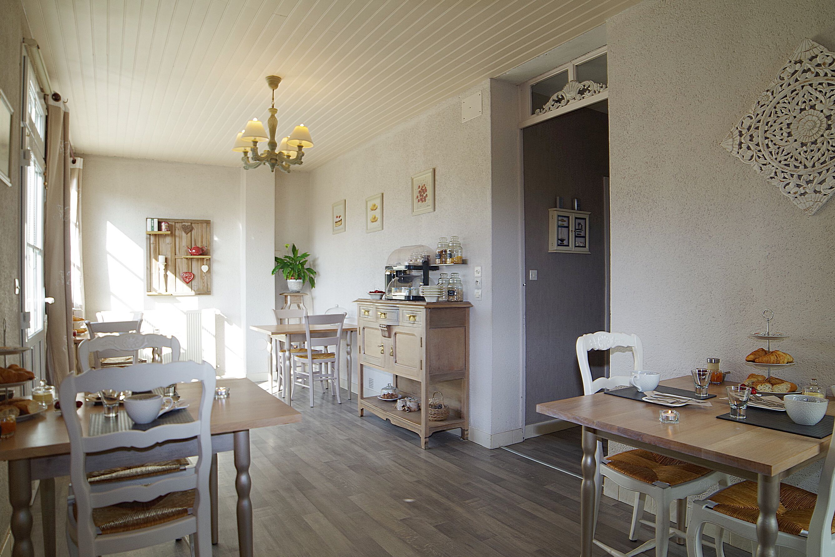 A dining area with wooden tables and chairs, a chandelier, and a wall-mounted decorative piece.