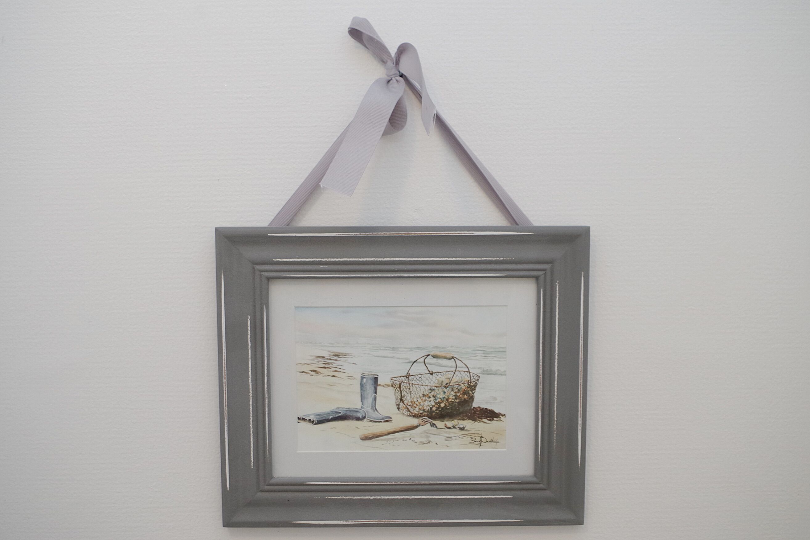 A framed artwork of a fishing net and boot on a beach.