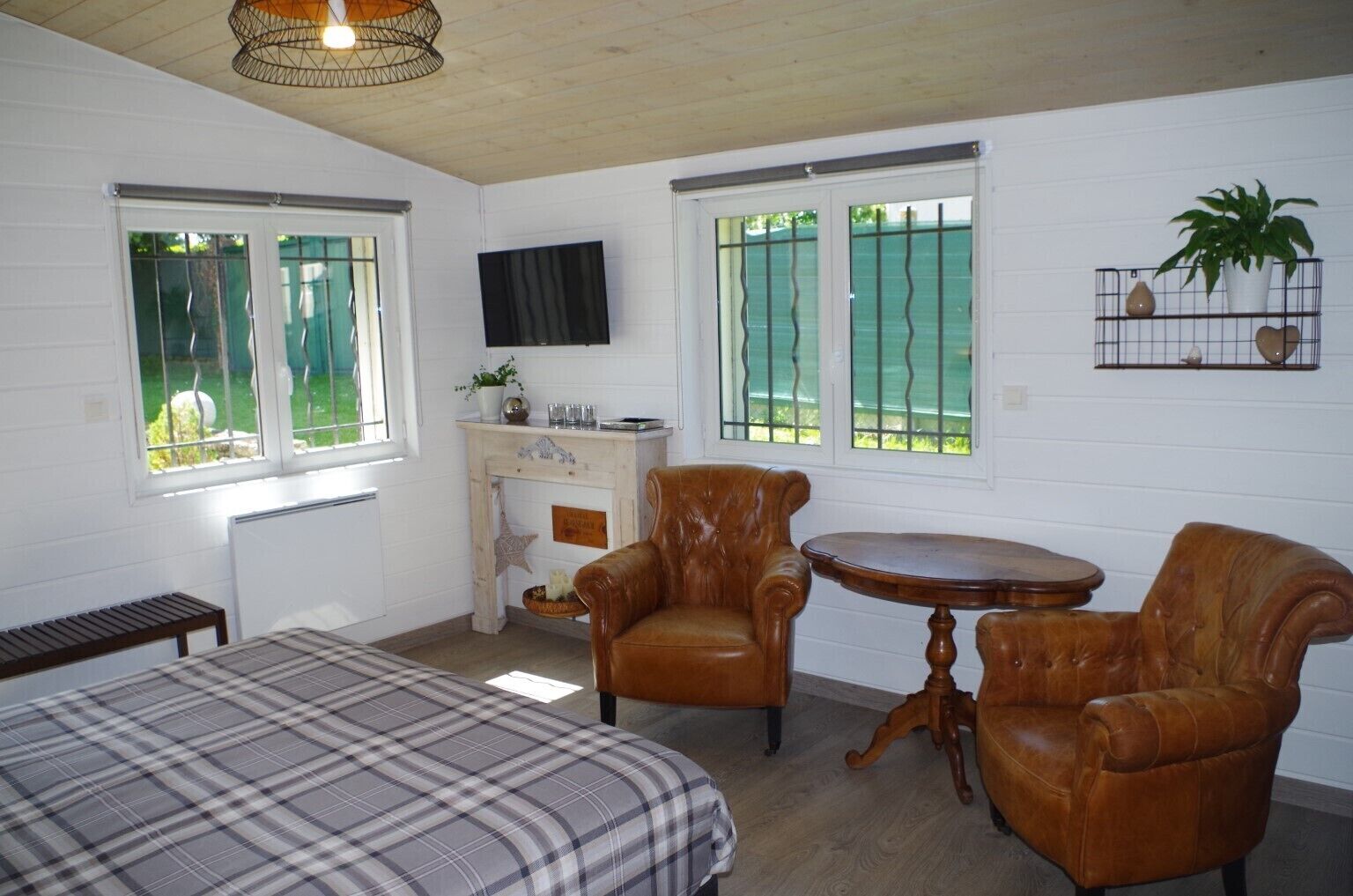 A room with a bed, two leather chairs, a small table, a fireplace, and a TV on the wall.