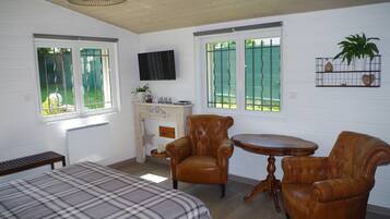 A room with a bed, two leather chairs, a small table, a fireplace, and a TV on the wall.