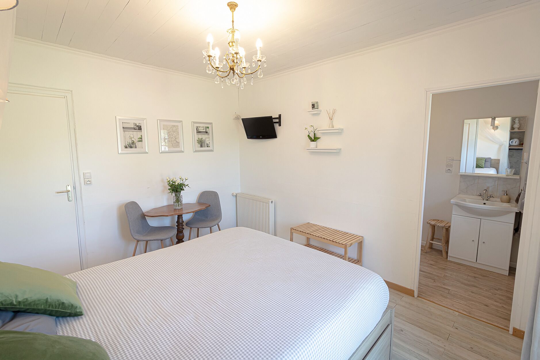 Un dormitorio con cama, escritorio y sillas, radiador, y baño con lavamanos y espejo.
