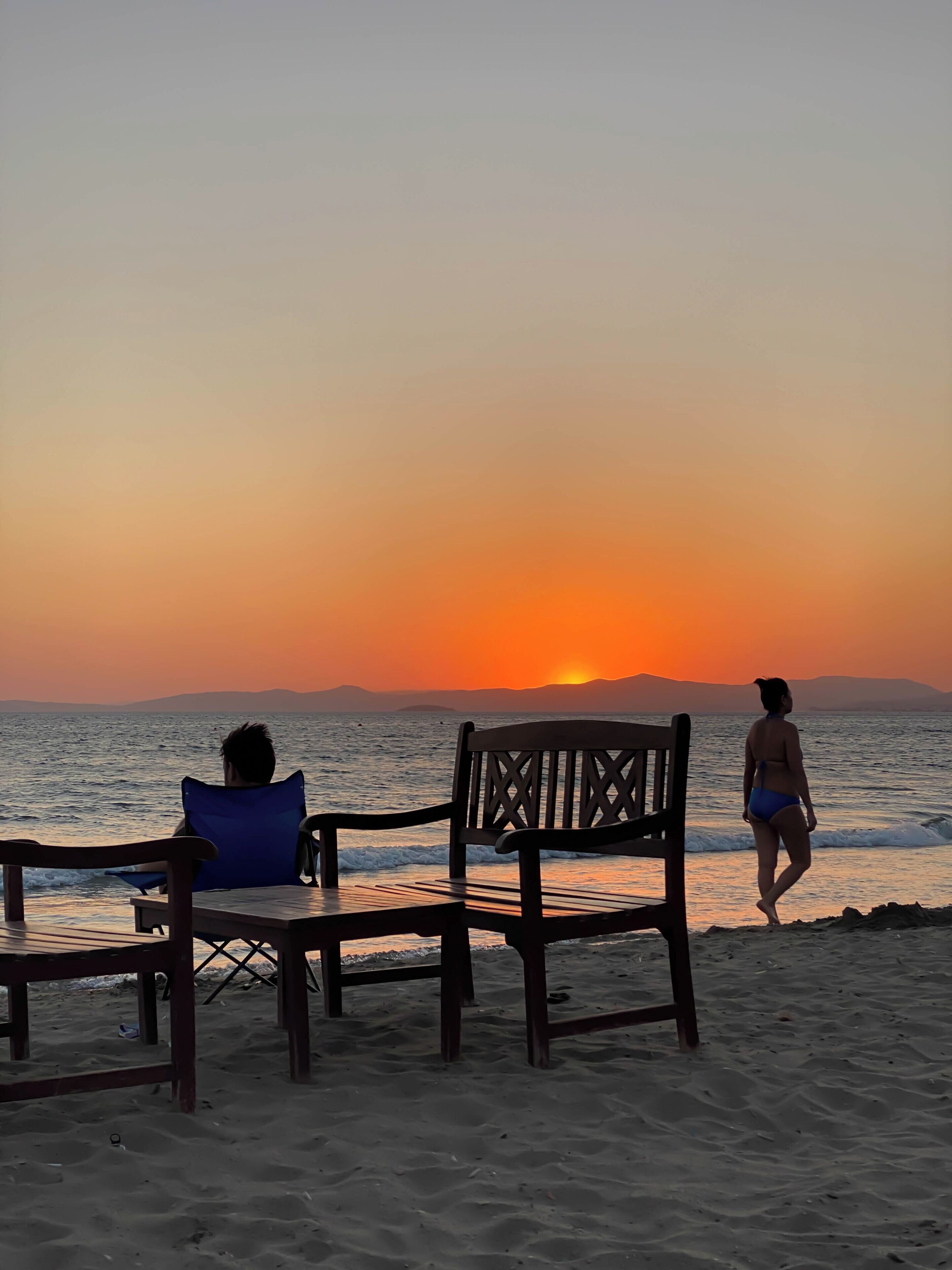 A beach scene with two wooden chairs and a person walking.