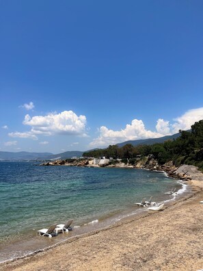 A beach with clear blue water, a rocky shoreline, and a few beach chairs. - Hermes Hotel Özdere (Menderes)