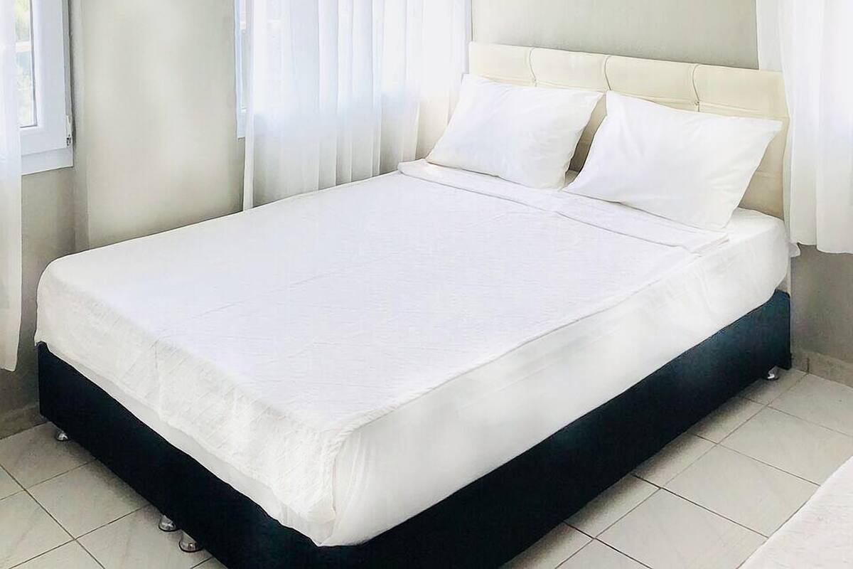 Een moderne hotelkamer met een groot bed, witte gordijnen en een paarse hanglamp.