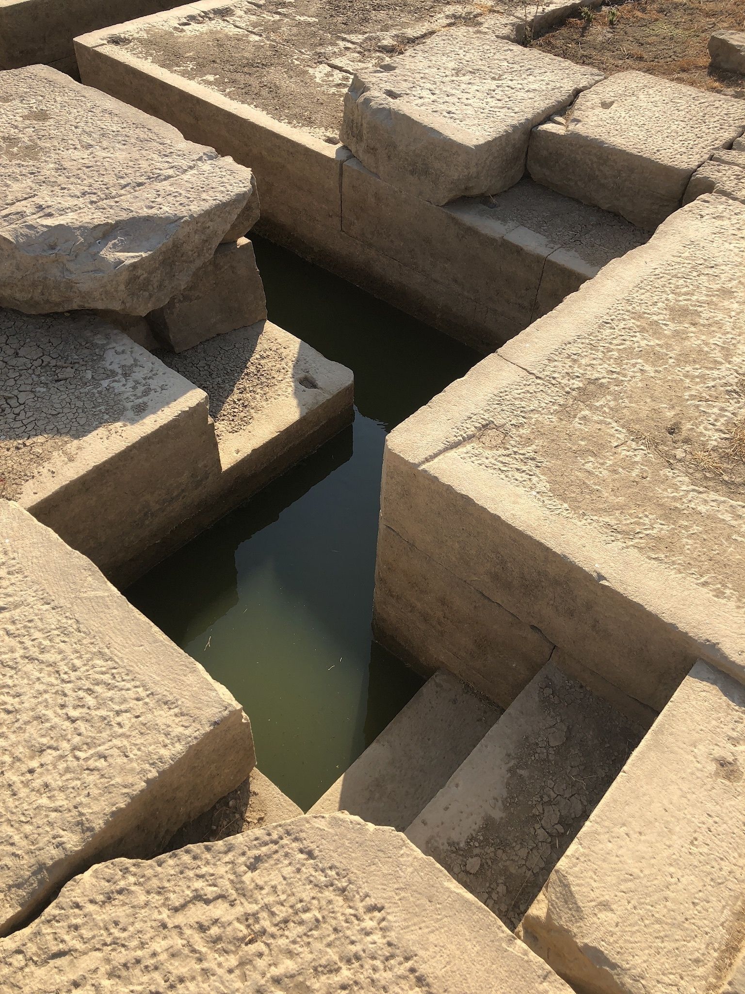 Une structure en pierre sèche et craquelée, avec une petite dépression remplie d’eau.