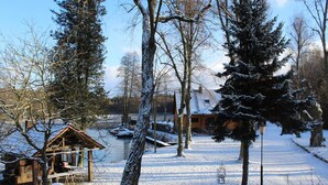 A rustic cabin with a snow-covered roof, surrounded by trees and a small dock. - Pension & Gasthaus Kattenstieg (Heiligengrabe)