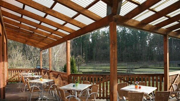 An outdoor covered patio with tables and chairs, overlooking a wooded area. - Pension & Gasthaus Kattenstieg (Heiligengrabe)