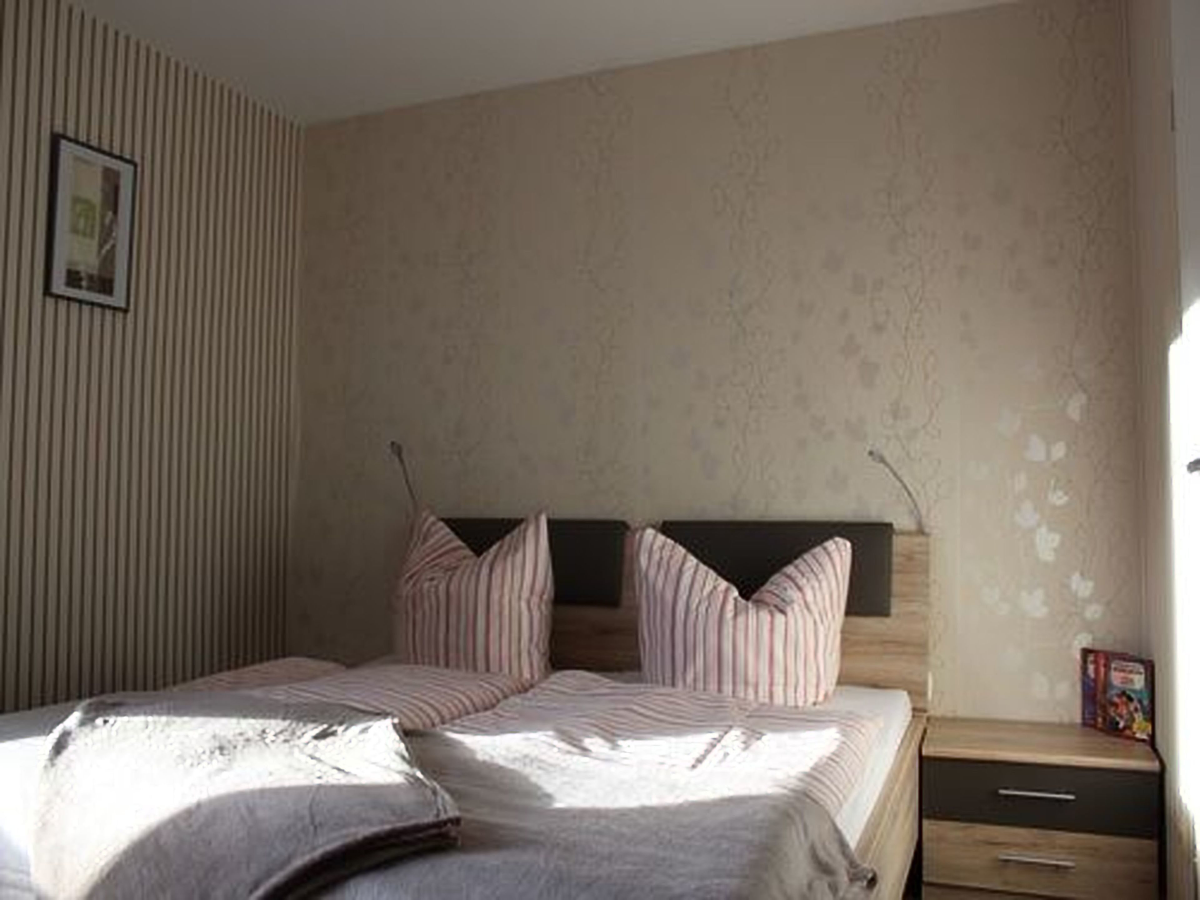 A bedroom with a bed, two pillows, a nightstand, and a framed picture on the wall.