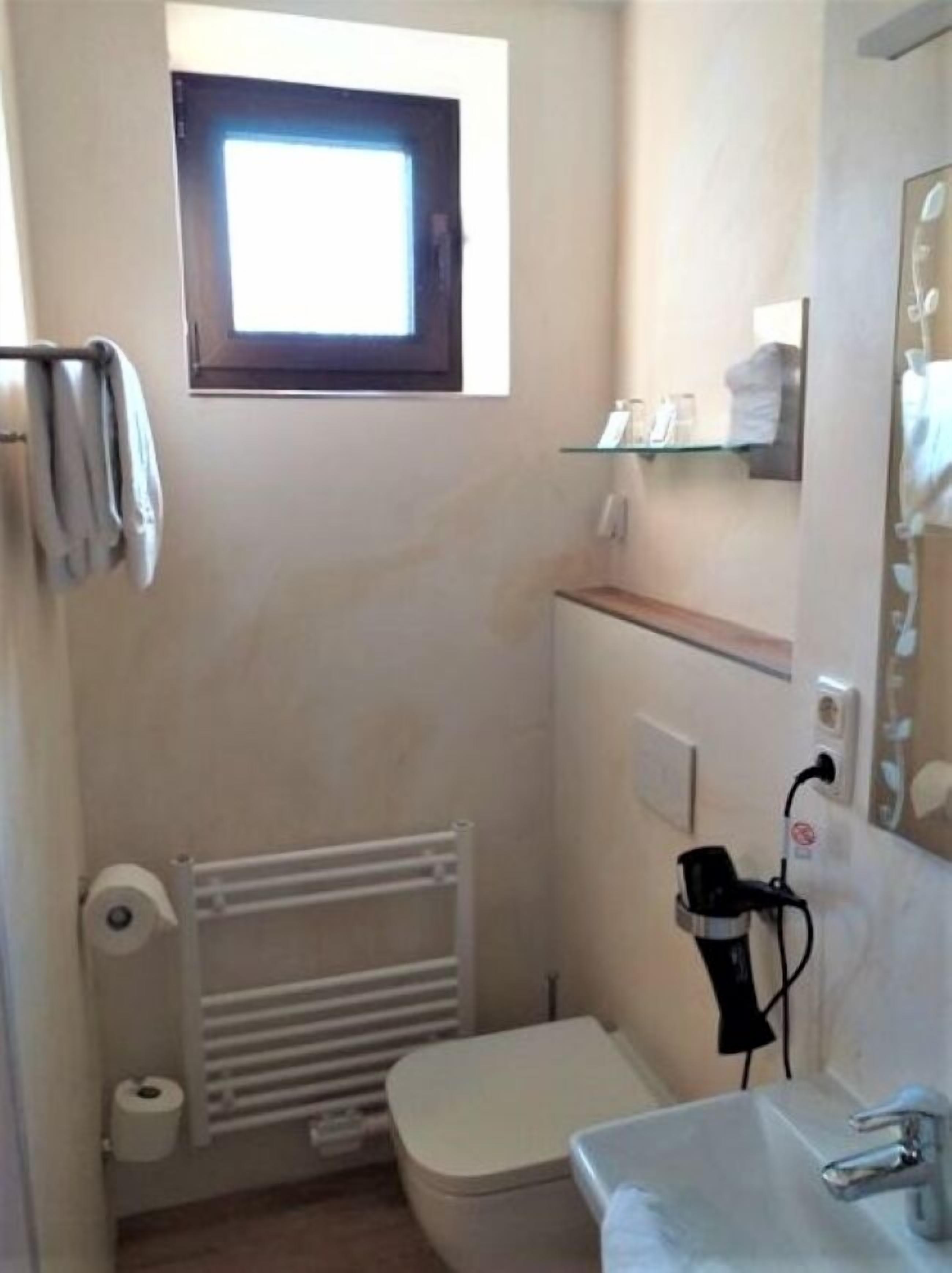 Un bagno piccolo e compatto, con il water, un lavandino, un appendi-asciugamani, una finestra e un termosifone.