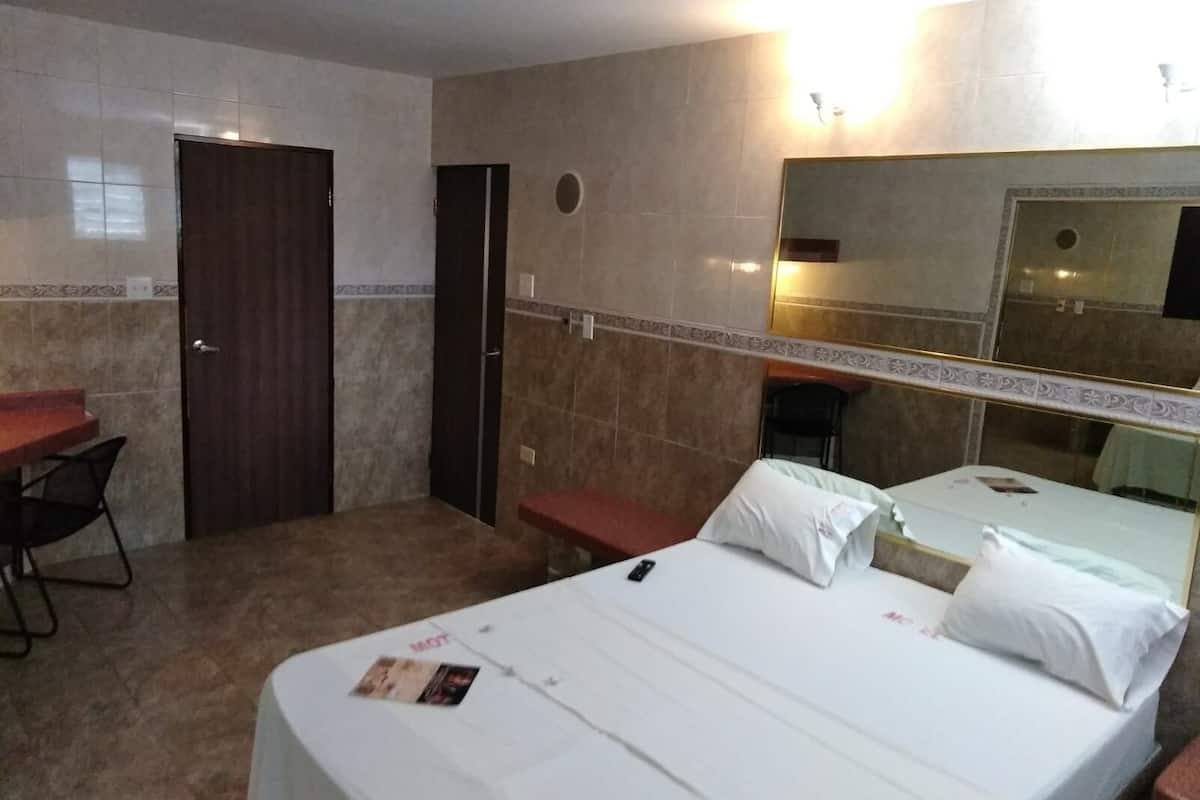A hotel room with a bed, a desk, a chair, and a mirror.