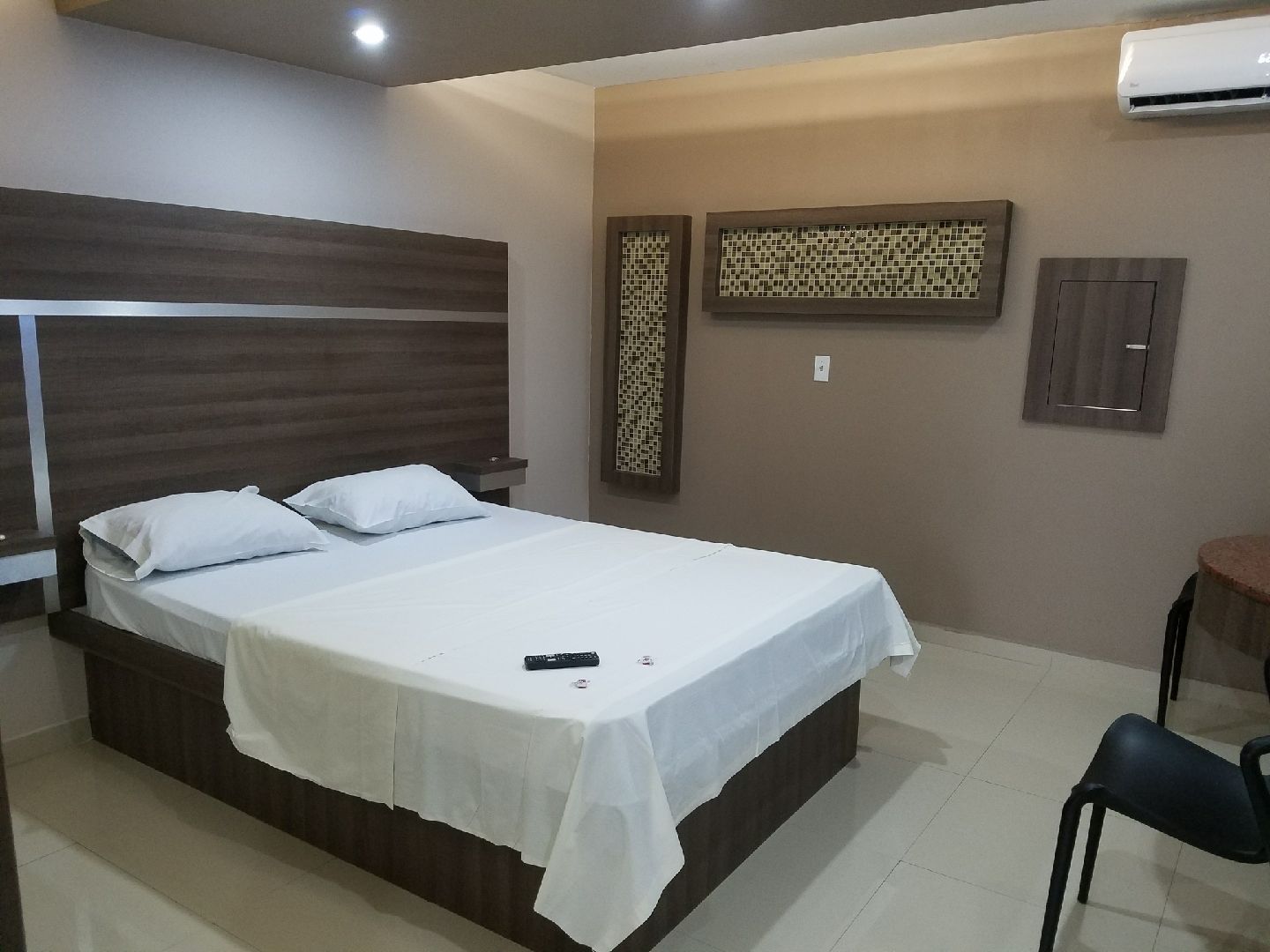 Habitación de hotel con una cama grande, una mesita de noche, una silla y un aire acondicionado instalado en la pared.