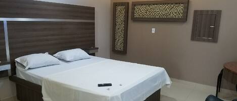 Habitación de hotel con una cama grande, una mesita de noche, una silla y un aire acondicionado instalado en la pared.