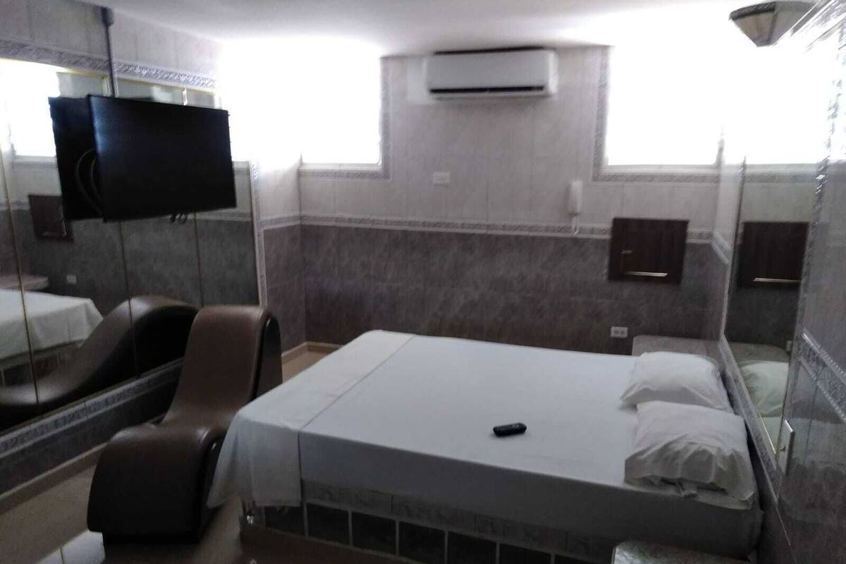 A hotel room with a bed, a TV, a chair, and a small bathroom.