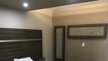 Habitación de hotel con una cama grande, cabecera, unidad de aire acondicionado montada en la pared y una pequeña mesa con control remoto y teléfono.