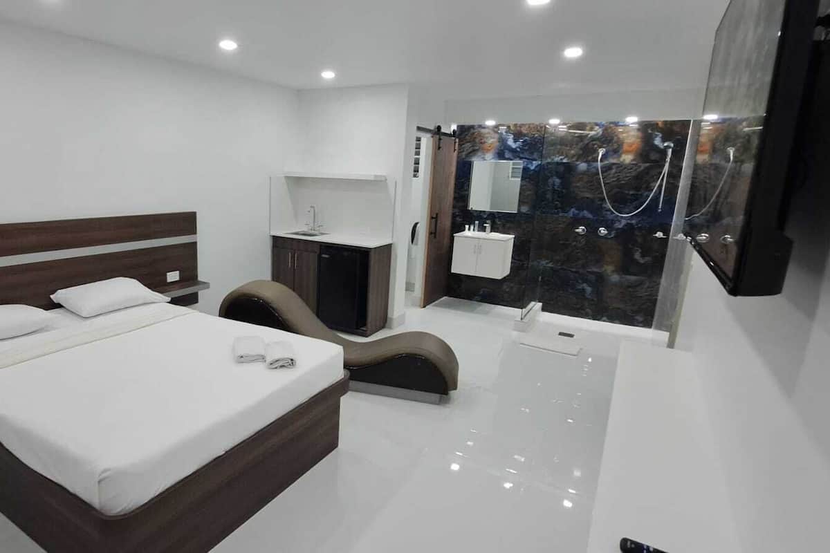 A modern bedroom with a large bed, a vanity with a mirror, and a shower area.