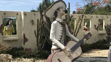 Una estatua de un hombre con traje blanco tocando una guitarra, frente a una pared con cactus y un cielo despejado.