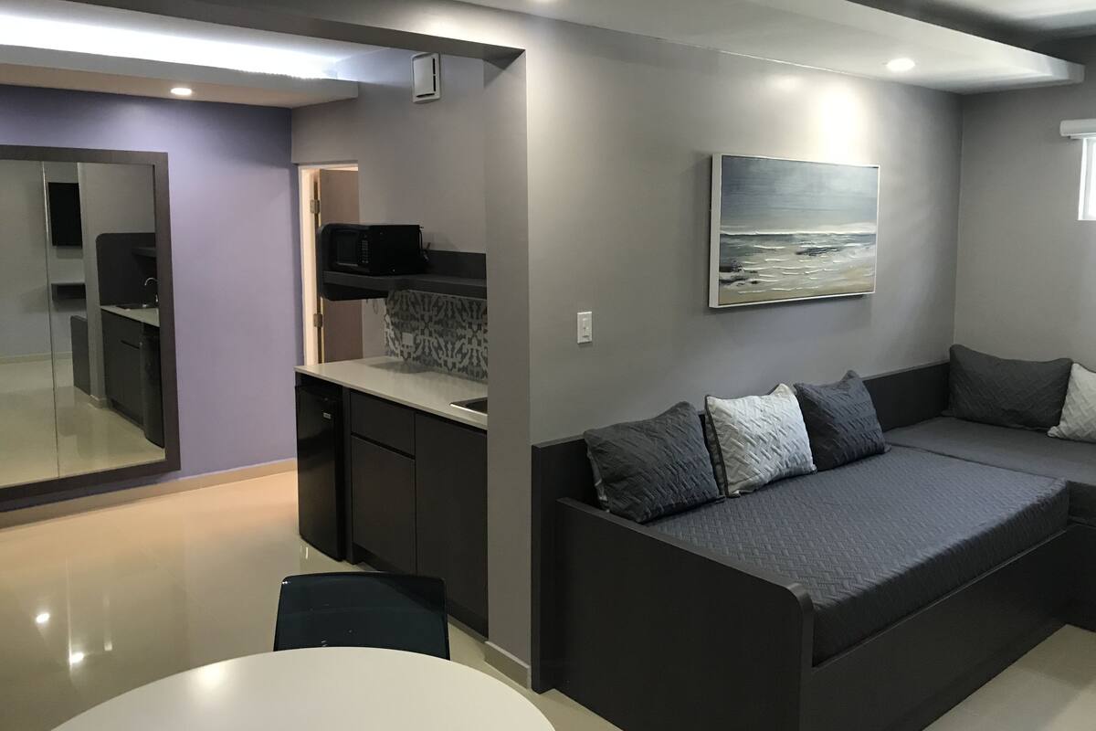 A modern living space with a kitchen area, a dining table, and a sofa with cushions.