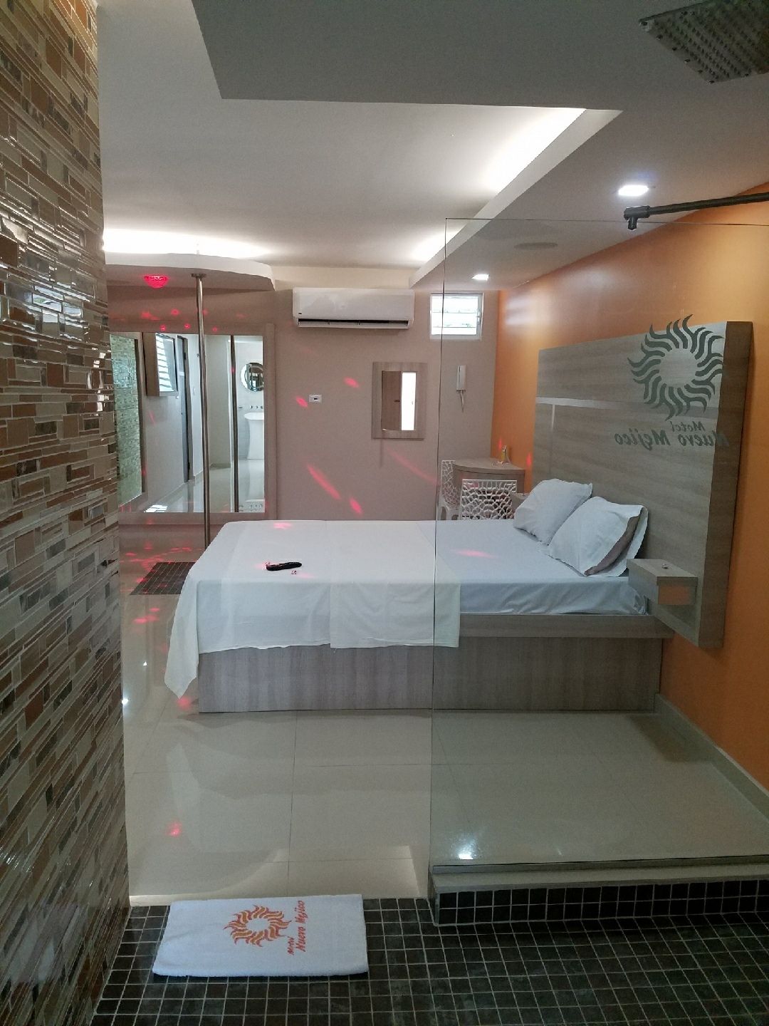 A modern hotel room with a large bed, a glass partition, and a view of the outside.