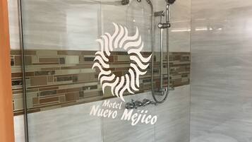 A modern shower with a glass door, a showerhead, and a handheld shower attachment. The shower is part of a room with a tiled floor and a decorative tile border.